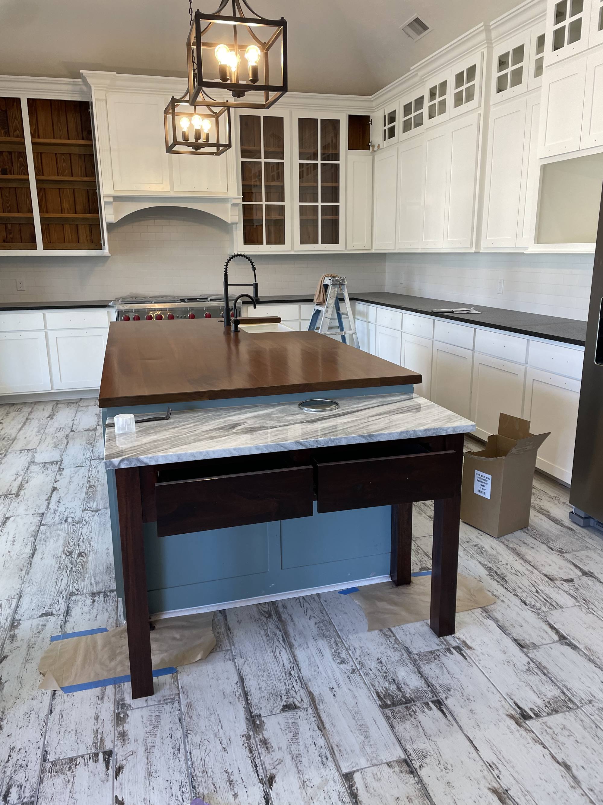 Custom kitchen showing the walnut-topped island, marble counters and painted cabinetry during finish work