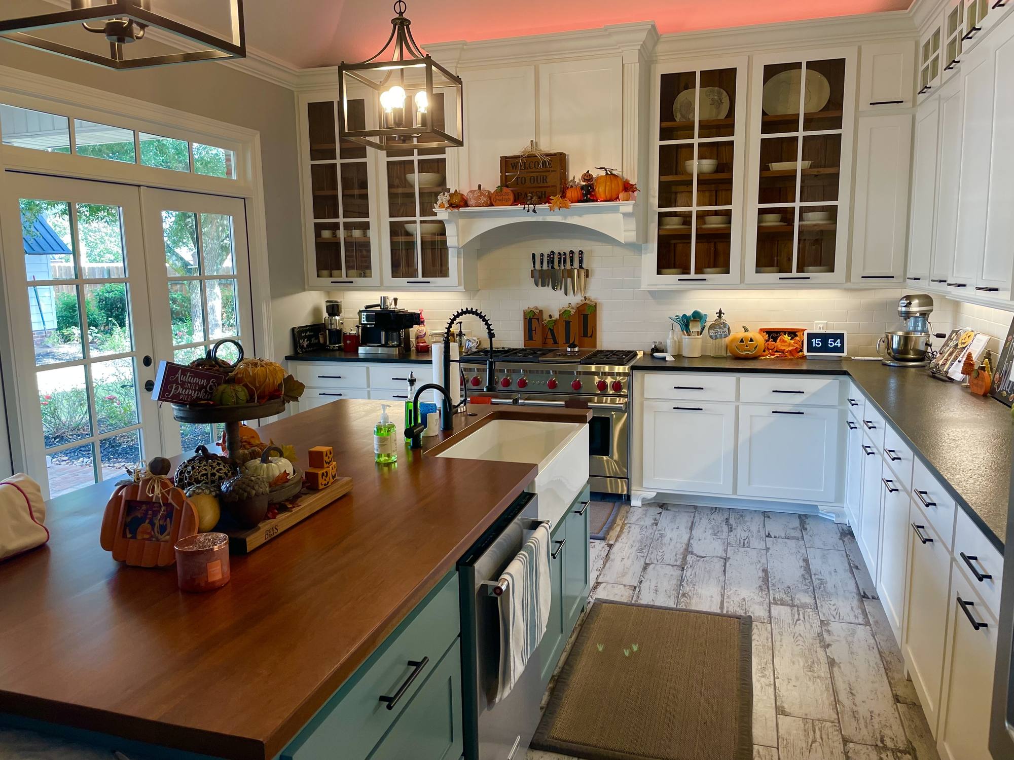 Custom kitchen with white painted cabinets, glass-front uppers, a painted hood surround and a walnut-topped island