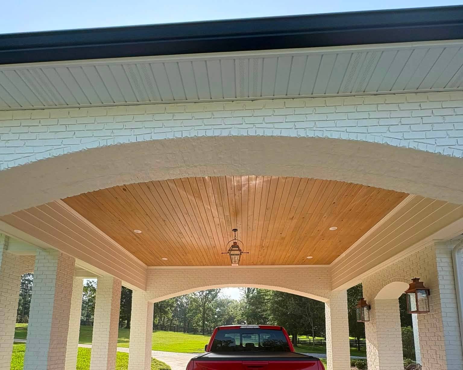 Barrel-vaulted cypress ceiling inside a painted brick porte-cochere with arched openings