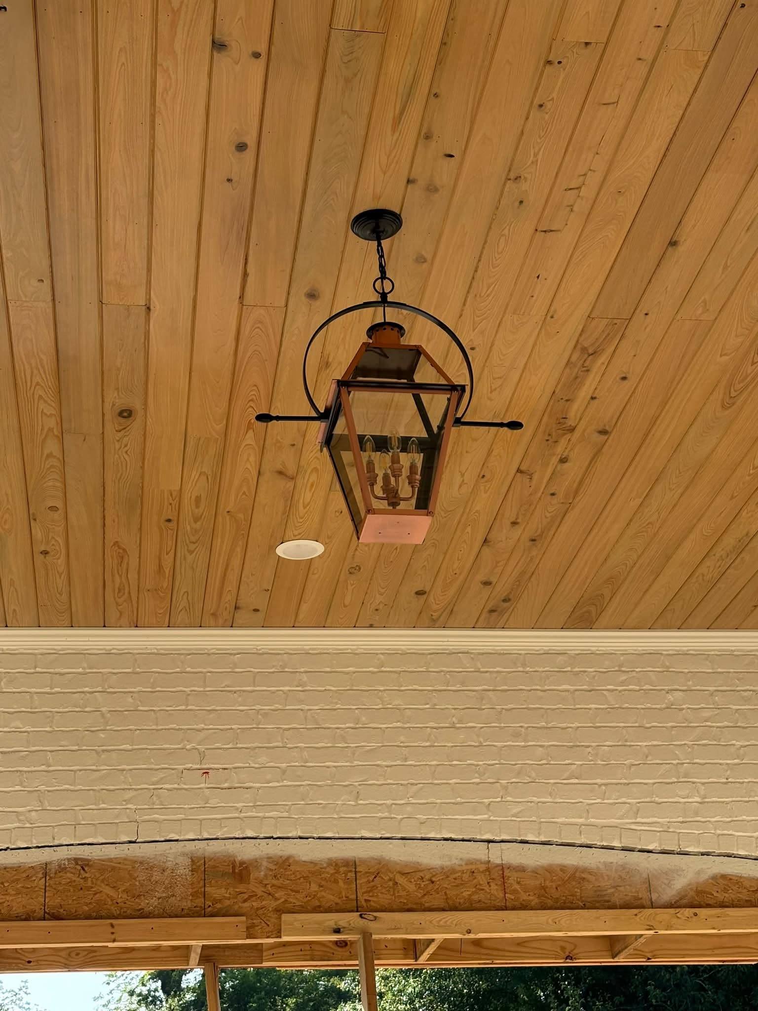 Tongue-and-groove cypress porch ceiling with a hanging copper gas lantern above painted brick