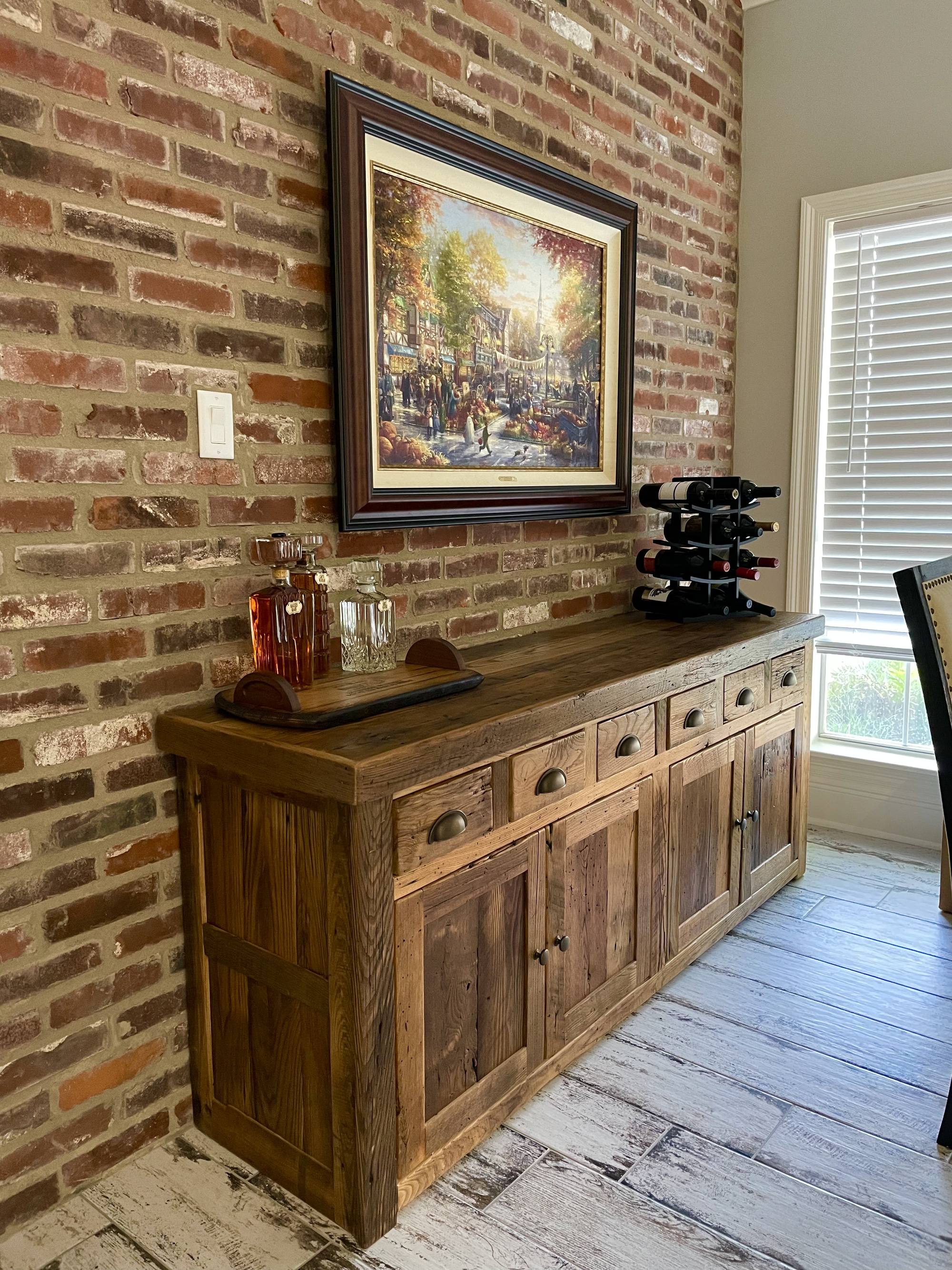 Custom reclaimed-wood buffet with drawers and panel doors standing against an exposed brick wall
