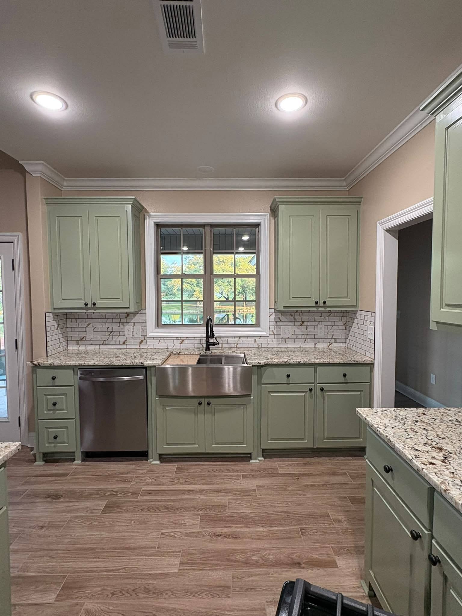 Sage green custom kitchen cabinets with a stainless farmhouse sink, granite counters and marble subway backsplash